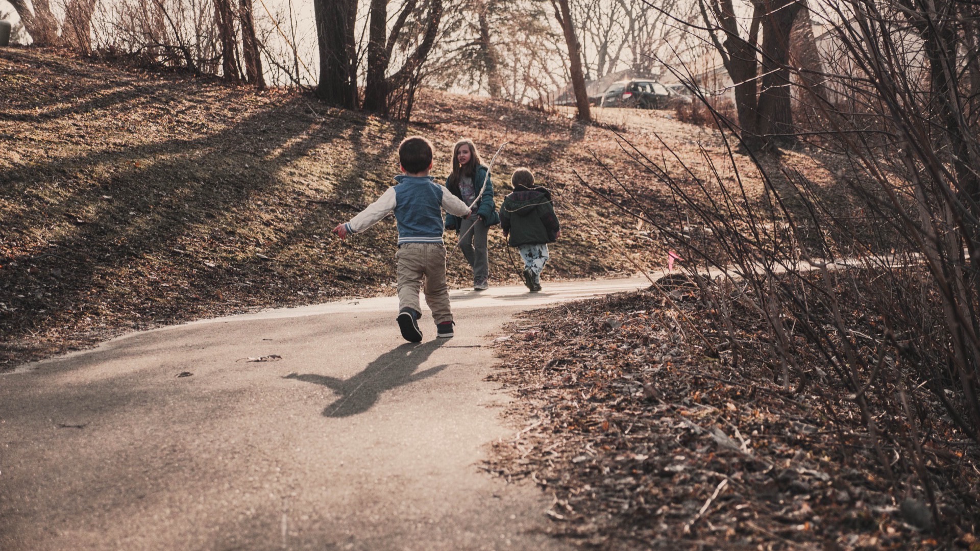 Children running ahead on a valley path, late-winter trees just beginning to bud